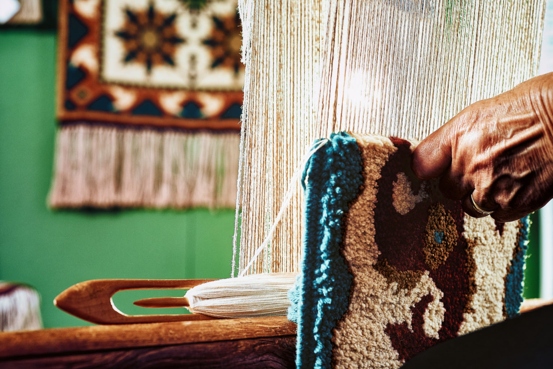 On the right in the picture is a hand that holds a fishing carpet with pattern. In the background you can see the fabric used for production